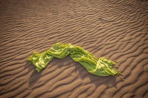 A green scarf lies on a wavy sand pattern